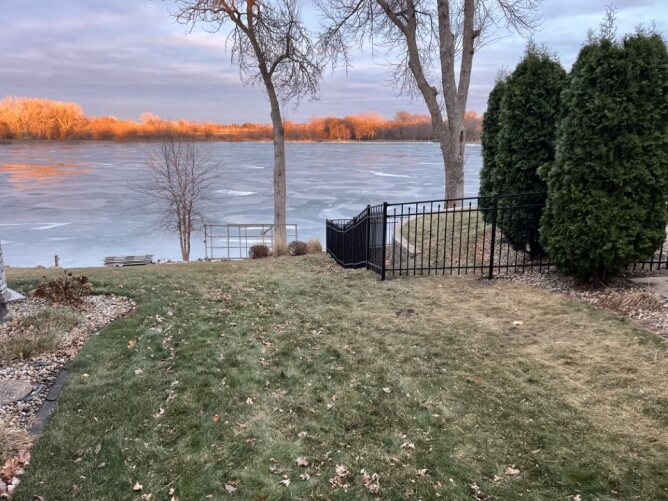 Black metal fence installed along a lakeside property with trees and a scenic water view in the background.