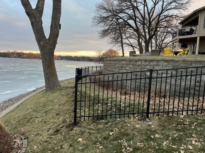 Black metal fence surrounding a landscaped residential yard with trees, shrubs, and lawn area.