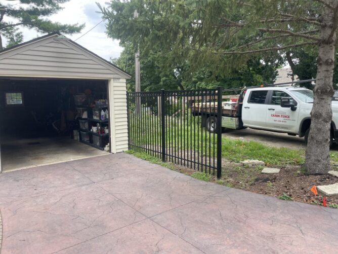 Black metal fence installed beside a driveway and garage with a parked truck in a residential setting.