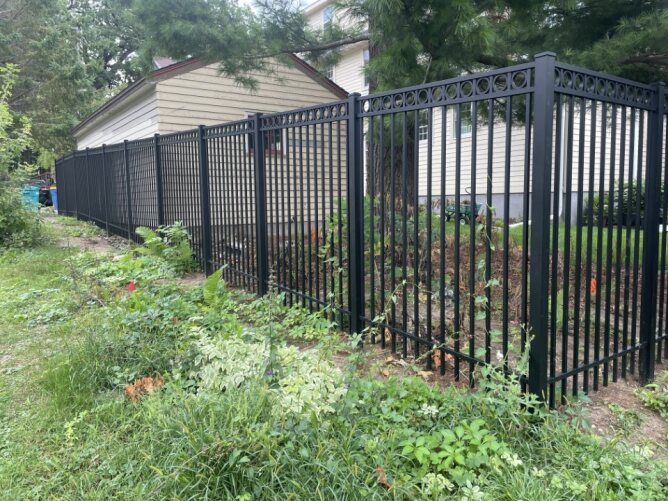 Black metal fence installed beside a driveway and garage with a parked truck in a residential setting.