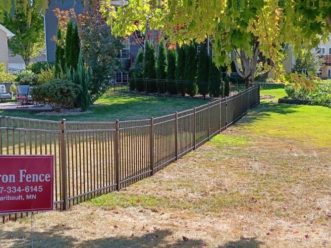 Black metal fence surrounding a landscaped residential yard with trees, shrubs, and lawn area.