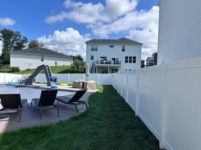 White vinyl privacy fence surrounding a backyard with a pool, lounge chairs, and residential homes in the background.