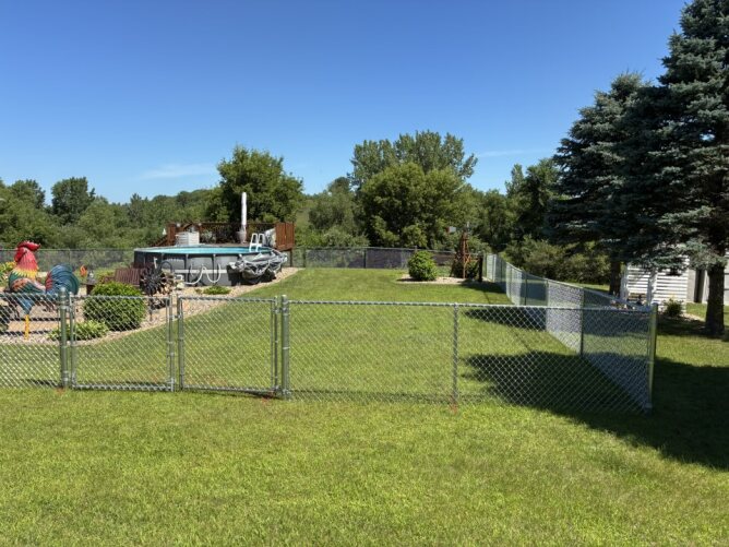 Black chain link fence installed along a grassy backyard with trees and a deck area in the background.