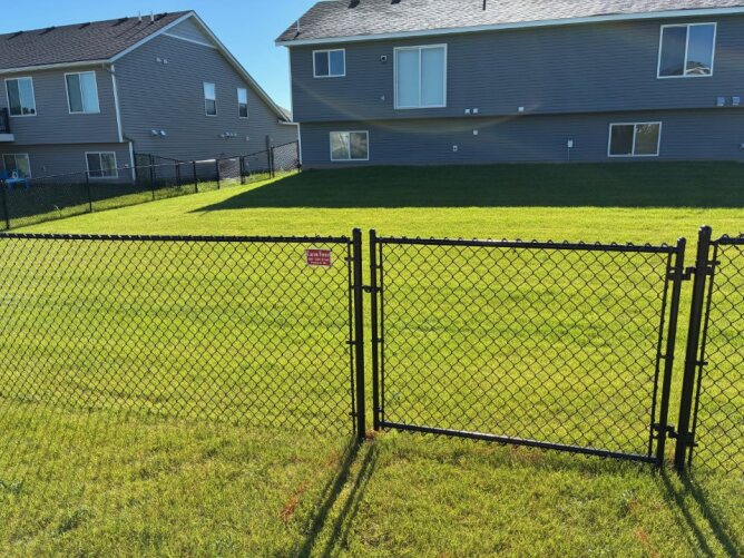 Chain link fence surrounding a large backyard with green grass, above-ground pool, and landscaping.