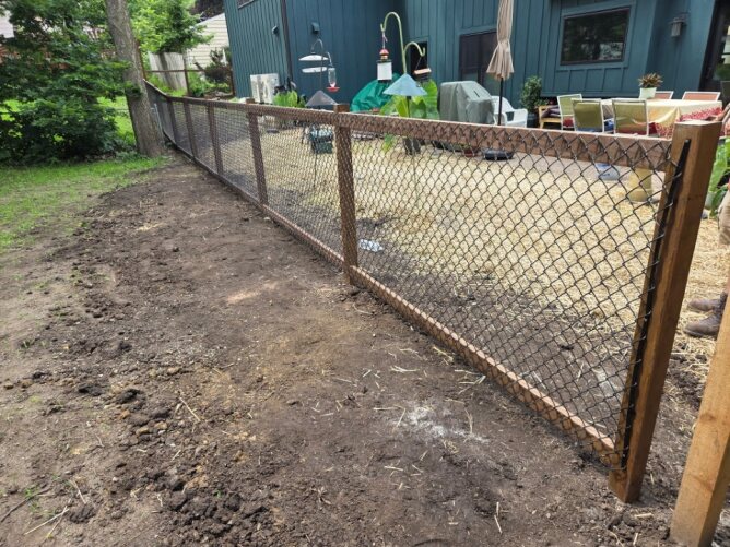 Horizontal wooden privacy fence with black metal posts installed along a residential sidewalk with trees and landscaping.