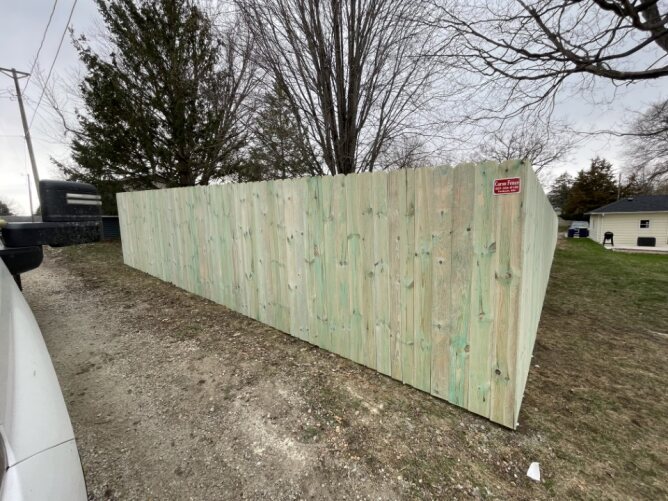 Newly installed wooden privacy fence along a residential property with dirt ground and trees nearby.