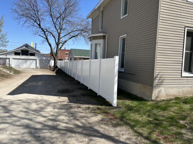 White vinyl double gate installed on the side of a house with a grassy backyard and neighboring homes.