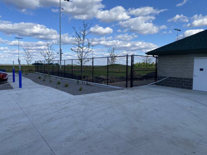 Black chain link fence installed around a commercial outdoor area near a parking lot and building with landscaped surroundings.