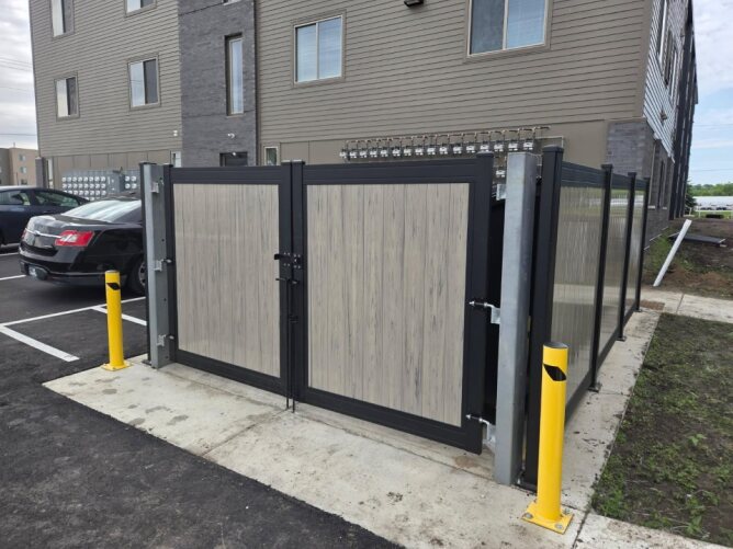 Commercial metal fence with double gate and privacy panels installed in a parking area beside a building.