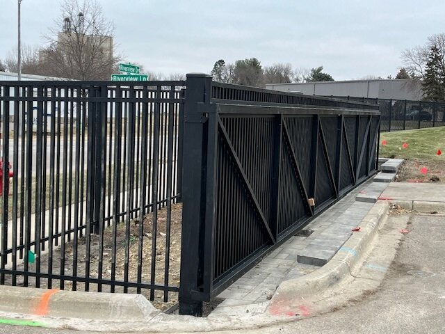Commercial black metal fence with sliding gate installed along a roadside for security and access control.