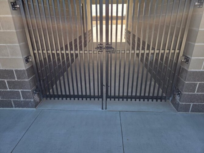 Secure vertical metal gate installed between concrete block walls, providing controlled access to a service area.