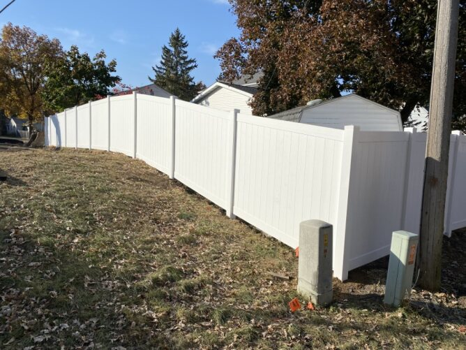 White vinyl privacy fence installed in a backyard with grass and trees, featuring a gate section.