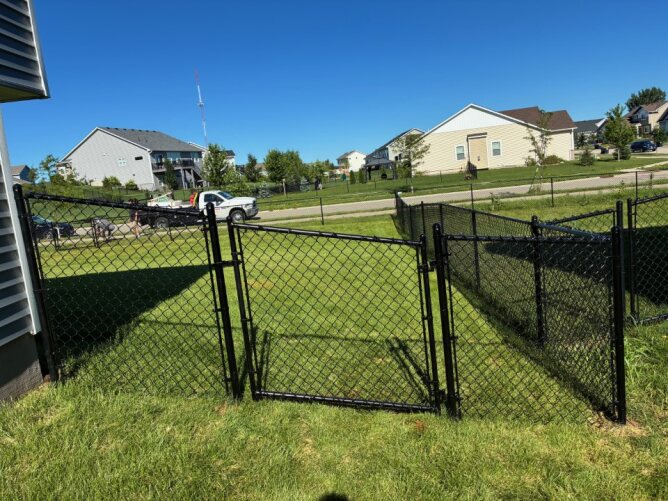 Chain link fence surrounding a large backyard with green grass, above-ground pool, and landscaping.