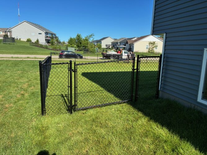 Chain link fence surrounding a large backyard with green grass, above-ground pool, and landscaping.