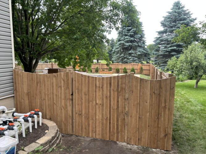 Newly installed wooden privacy fence along a residential property with dirt ground and trees nearby.