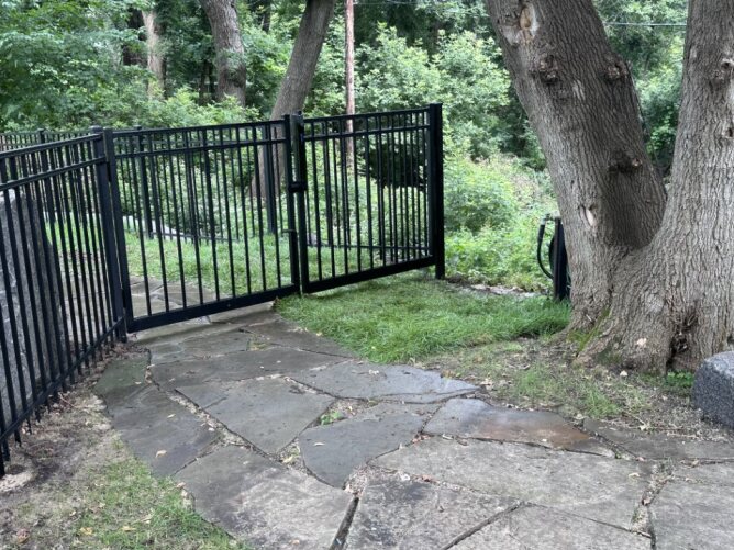 Black metal fence installed beside a driveway and garage with a parked truck in a residential setting.
