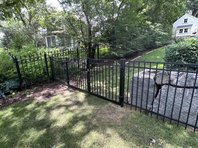 Black metal fence installed beside a driveway and garage with a parked truck in a residential setting.