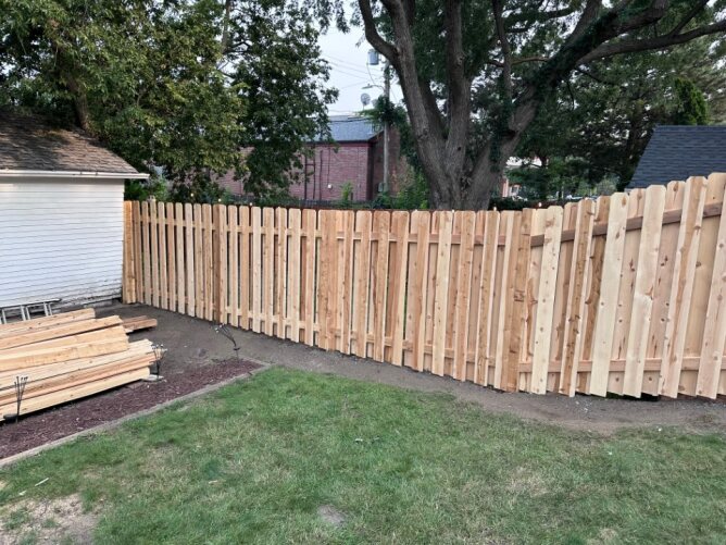 Newly installed wooden privacy fence along a residential property with dirt ground and trees nearby.