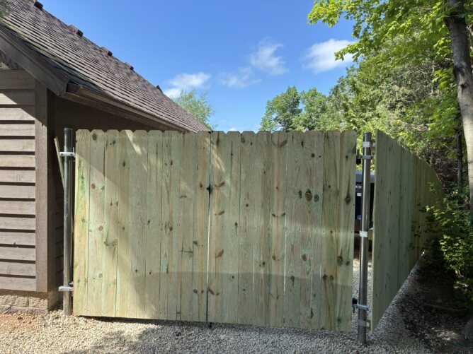 Newly installed wooden privacy fence along a residential property with dirt ground and trees nearby.