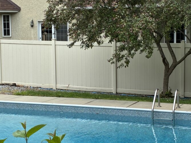 Gray vinyl privacy fence with gate installed between two houses, enclosing a small patio area with paver flooring.