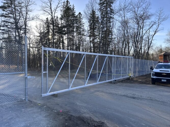 Large chain link fence with sliding gate installed in an outdoor area near trees.