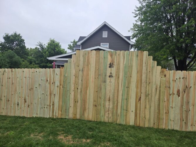 Newly installed wooden privacy fence along a residential property with dirt ground and trees nearby.