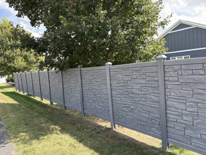 “Gray vinyl privacy fence with stone texture panels installed in a residential yard”